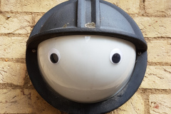 Wall-mounted outside light with eyes stuck on it to make it look like a person wearing a hat